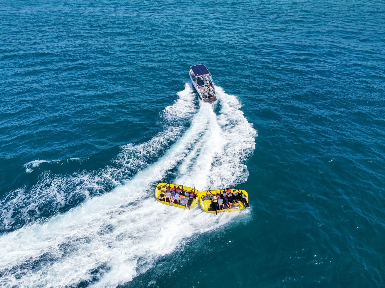 Aerial shot of a boat towing inflatables in the ocean, capturing a fun summer activity.